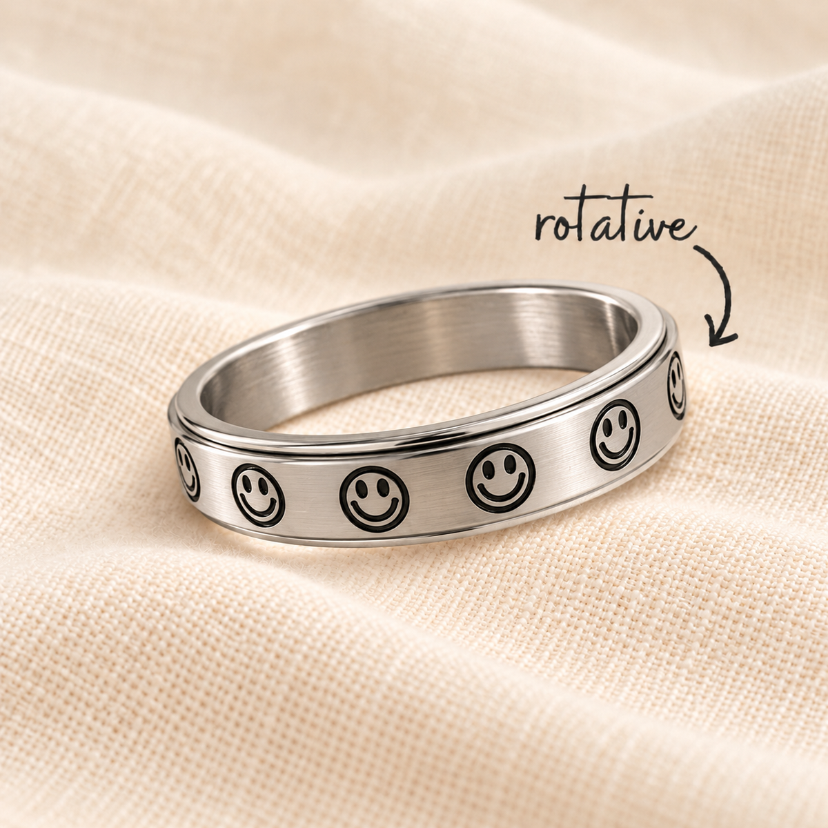 Bague Sourire argentée à motifs noirs sur lin crème avec flèche rotative
