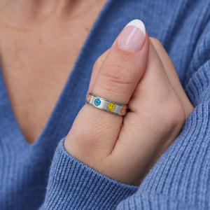 Bague Sourire coloré argentée portée au pouce avec un chandail bleu